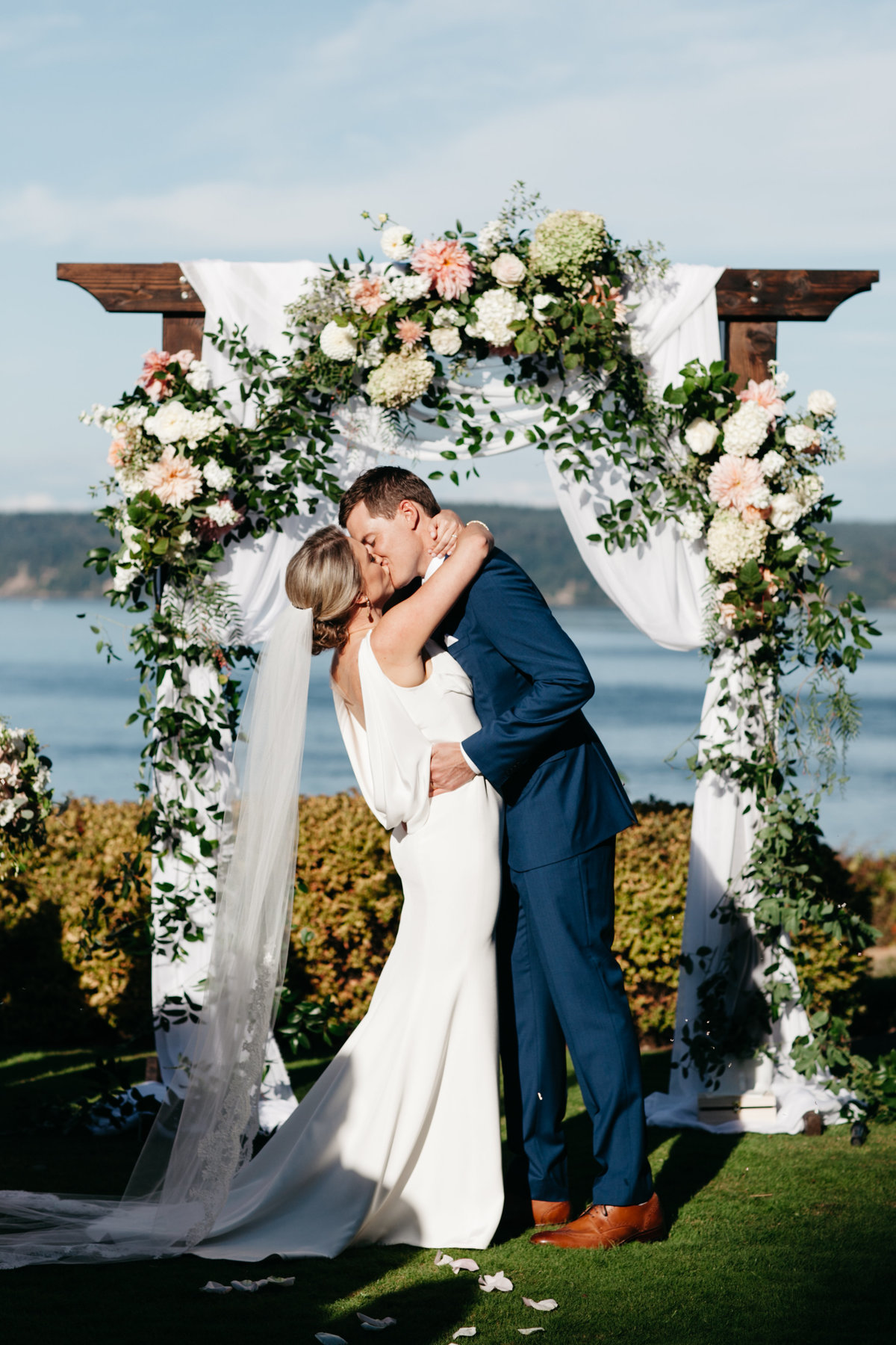 Wedding ceremony arch draped in white with blush flowers and smilax vines.
