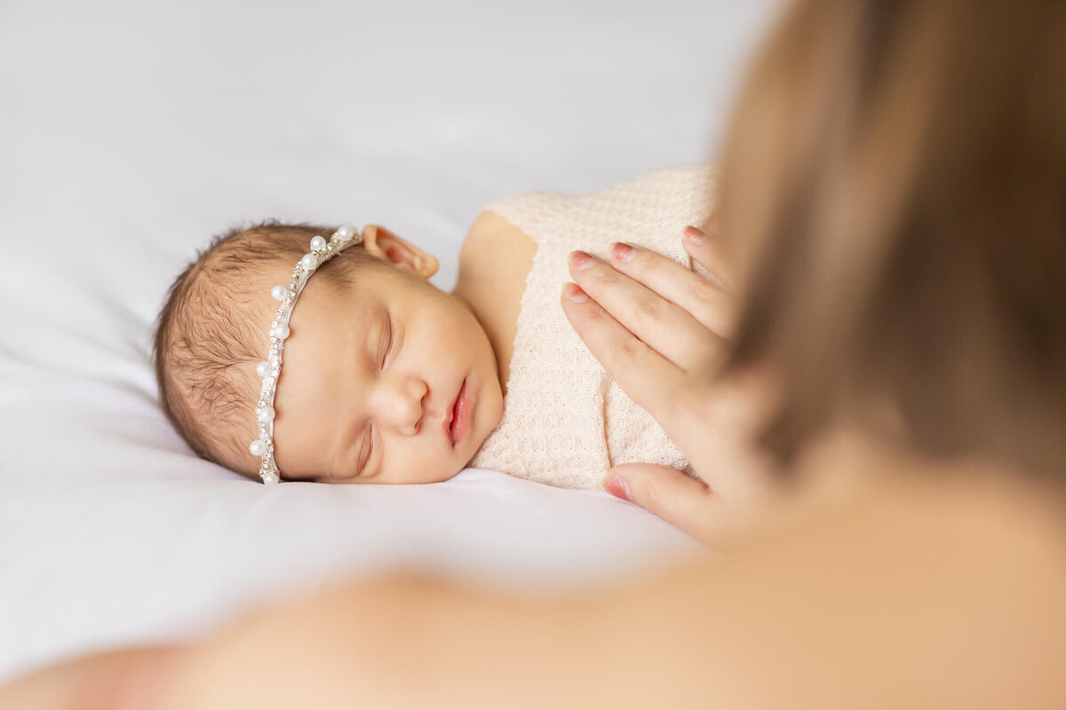 Newborn baby girl lays on the bed while mom looks at her and pats her