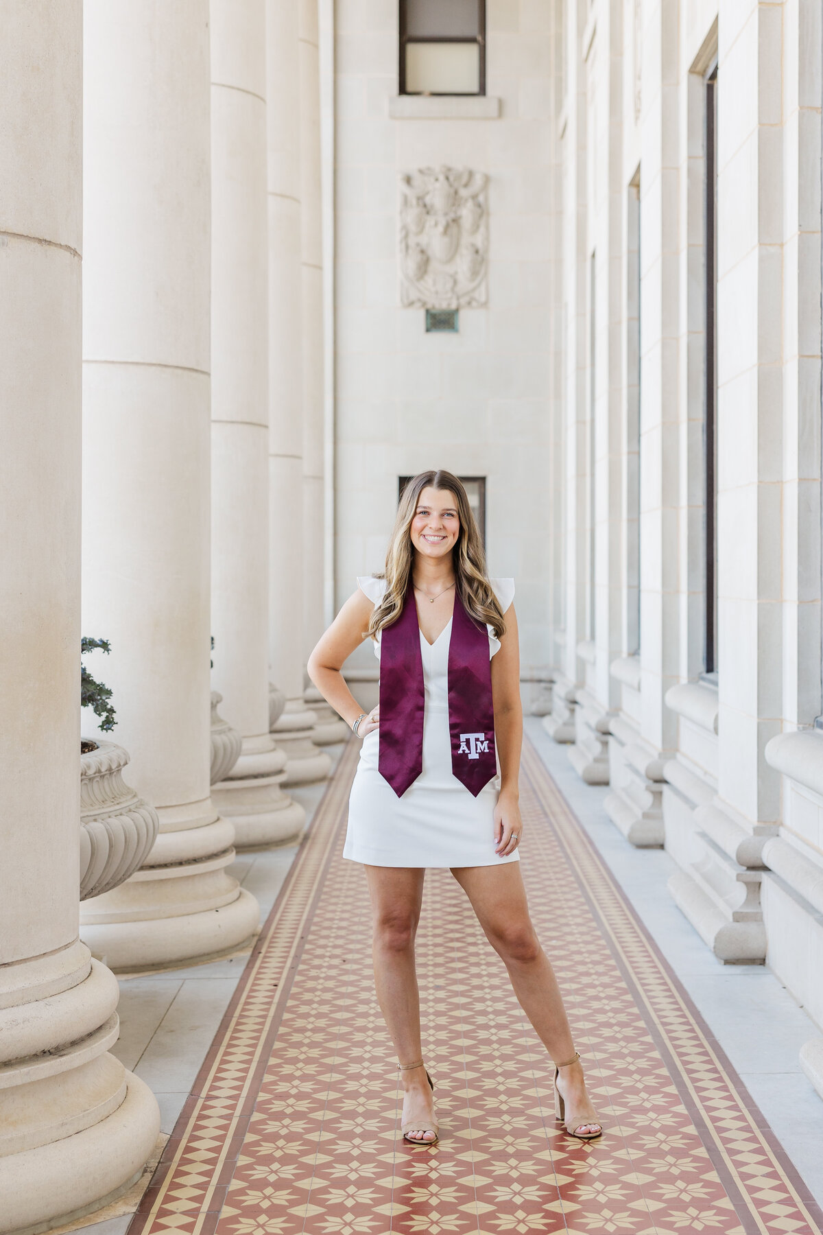 Full-length graduation portrait of an Aggie senior standing confidently in her maroon stole at Academic Plaza on the Texas A&M campus in College Station.