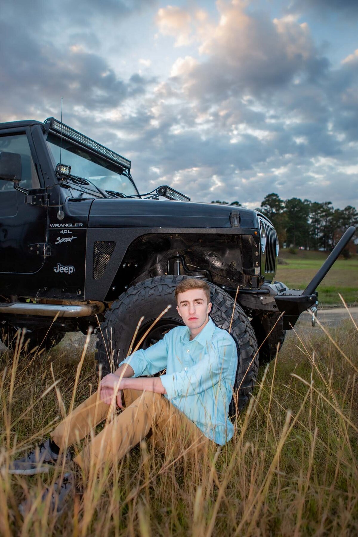 Senior portrait of a boy with his jeep in a wheat field at sunset.