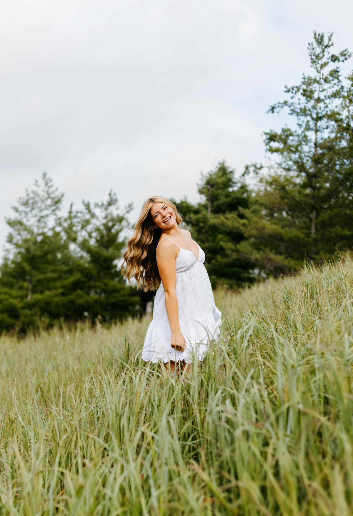 Senior girl in a white dress posing in a big grassy field