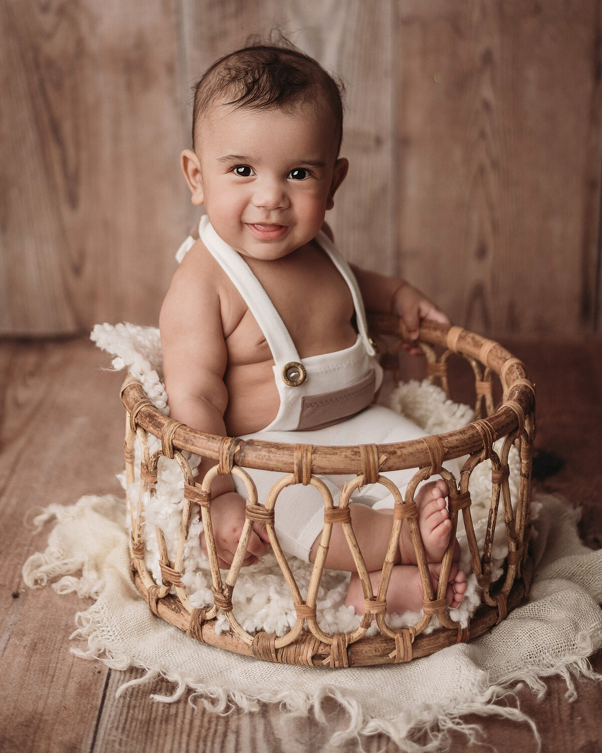 Stamford CT photographer captures portrait of happy baby boy wearing white overalls sitting inside a round wooden basket
