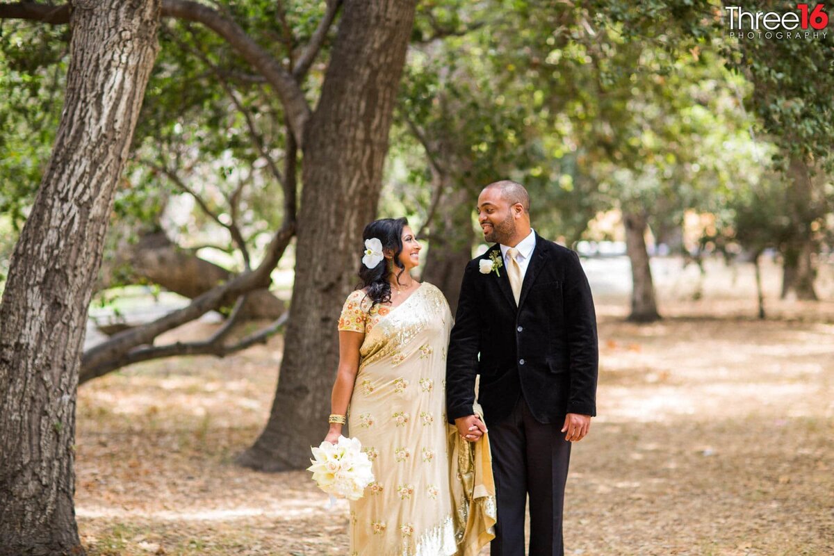 Bride and Groom walk amongst the trees while holding hands