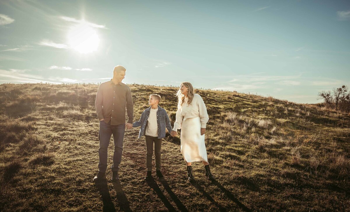 father and mother holding their middle school son walking down a hill at sunset