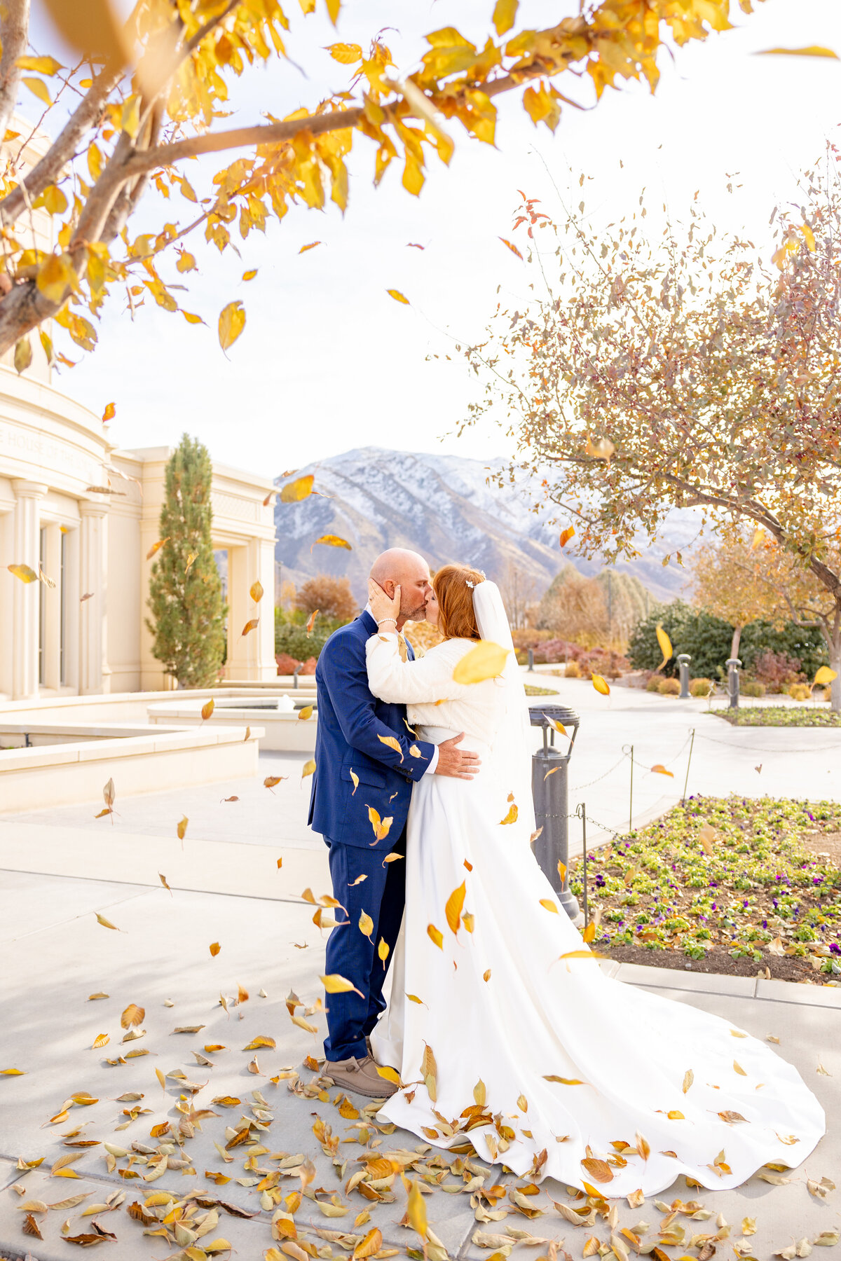 husband and wife share a kiss surrounded by the falling leaves in Autumn at the Payson LDS Temple