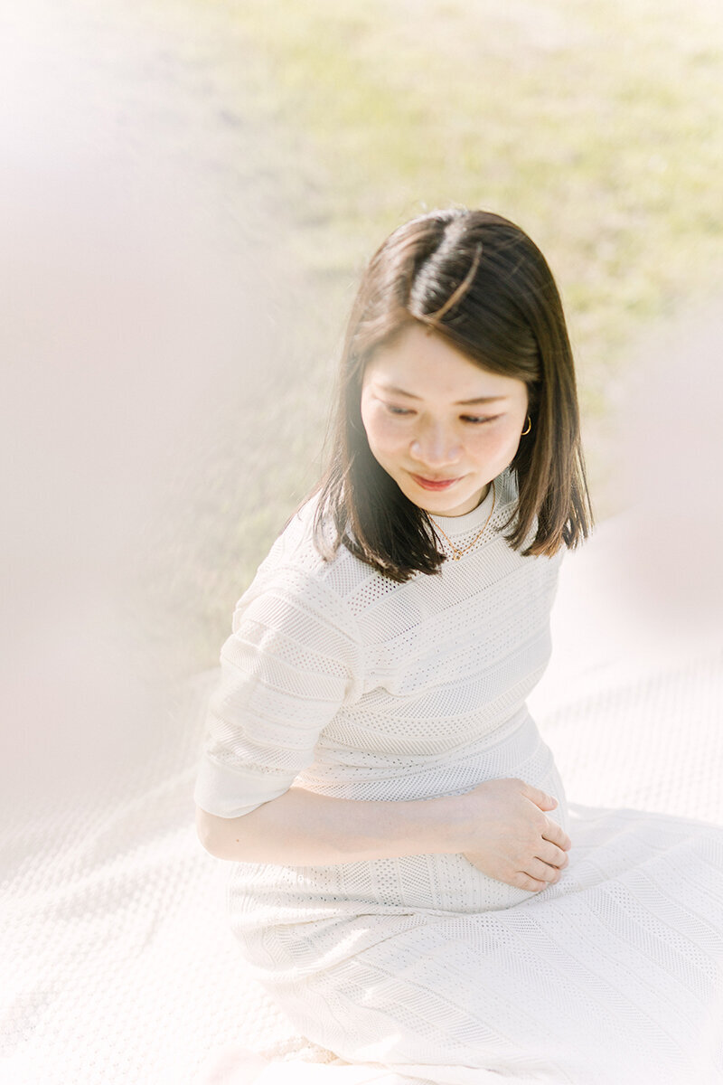 妊婦さんが座って、おなかに手を当てている、明るくて美しいおしゃれなマタニティフォト。
