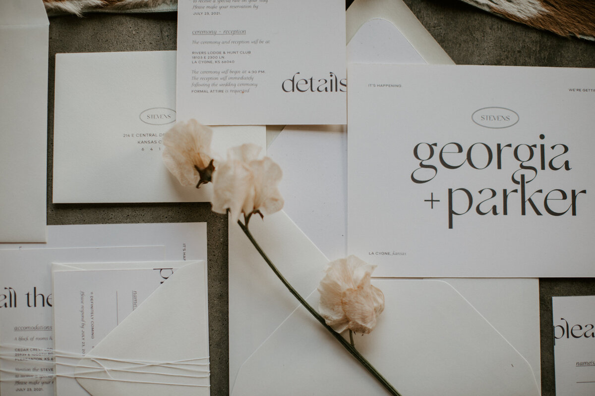 Various white wedding stationery with brown font and flower atop brown and white cow hide.