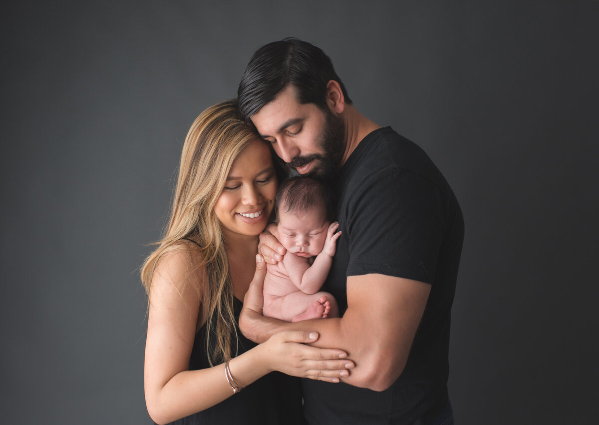 a mom and her husband holding baby with a black backdrop