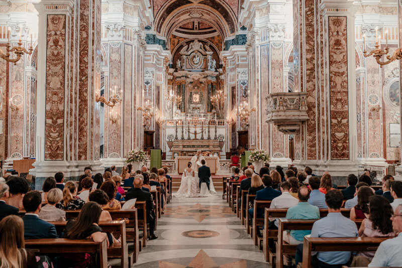 Cérémonie de mariage en Italie dans la cathédrale de Monopoli, avec un couple entouré de lumière et d’architecture baroque.