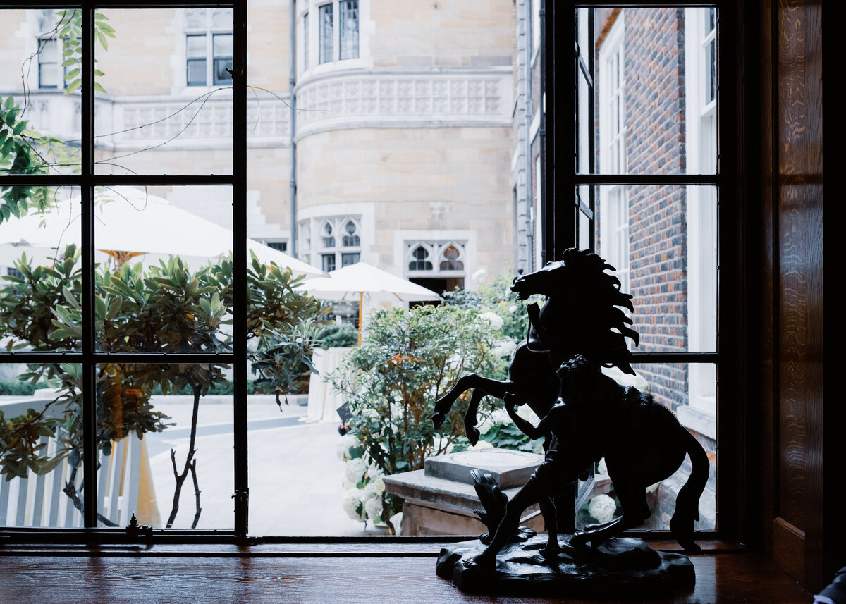 A rearing horse sculpture by a metal framed window overlooking a courtyard at a luxury london wedding.