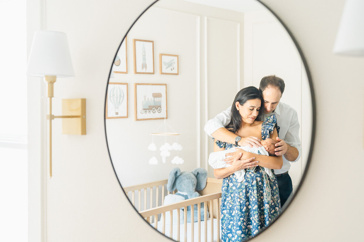 parents stand in front of a mirror in their newborn's nursery while being captured through the mirror by their Leander photographer.