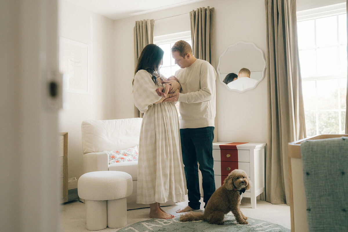 New mom and dad holding their newborn baby in a softly lit nursery during an in-home photography session