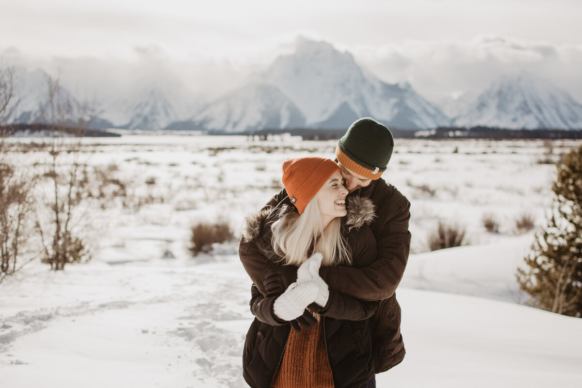 man holding woman from behind with his arms around her shoulders in the Grand Tetons for their winter engagement session