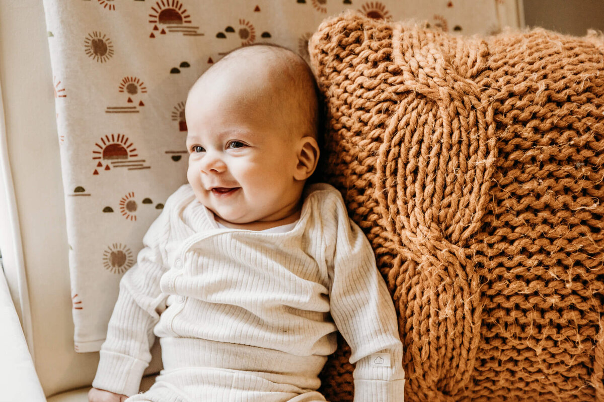Baby boy smiling while he sits up with pillow in Milwaukee home