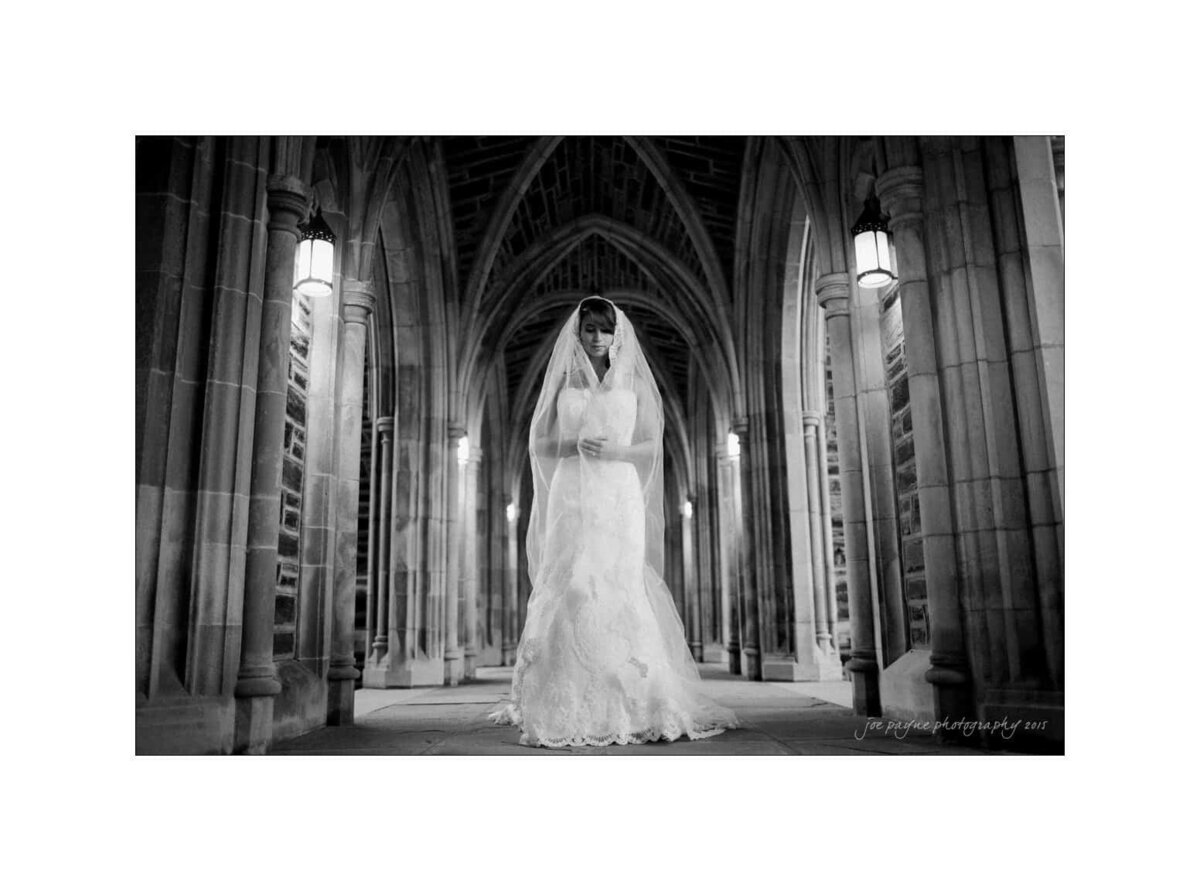 A bride with her veil around her as she stands in a grand corridor.