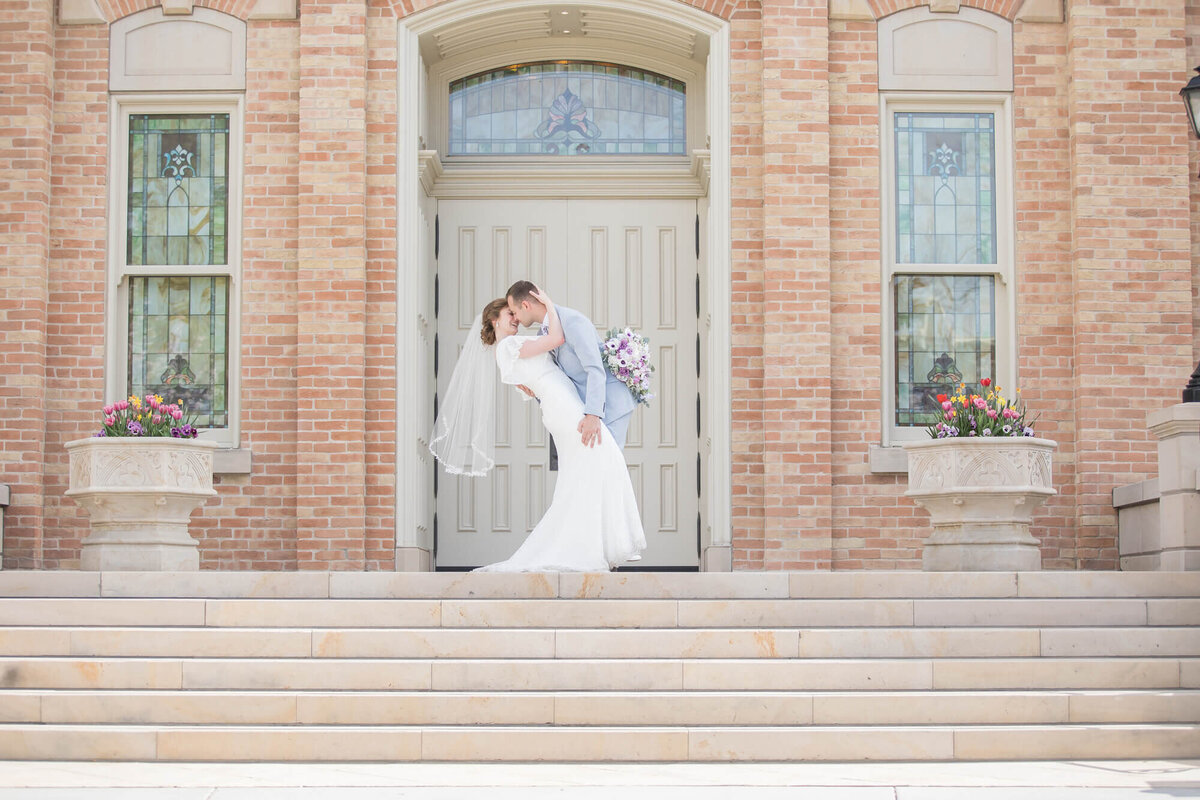 Groom dipping and kissing bride on the steps of a brick building, by las vegas wedding photography by Jessica