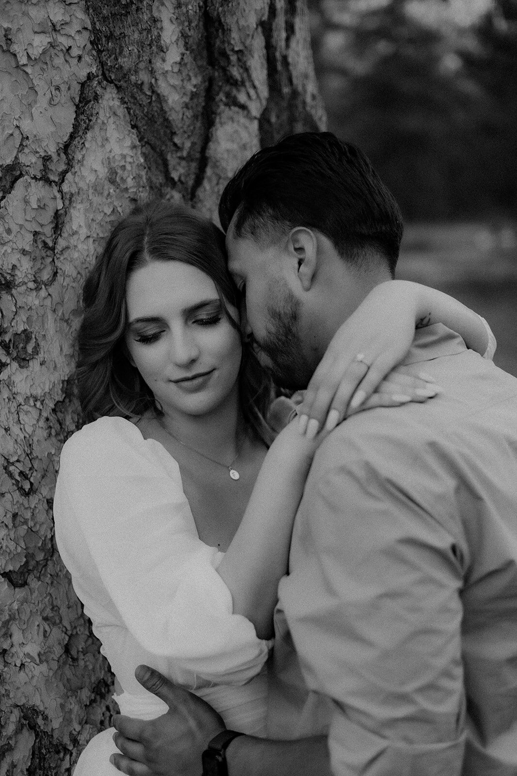 A black-and-white, intimate shot of the couple leaning against a tree, with the woman’s eyes closed as she rests her hand on his shoulder.