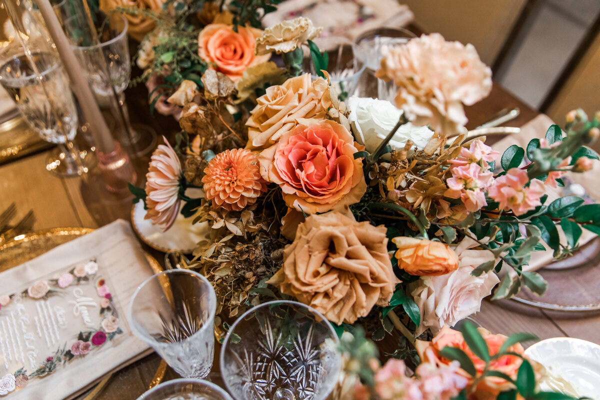 Beautiful fall floral centerpieces warm this reception space with a sunset color palette. Garden roses, ranunculus, double brownie tulips, and lisianthus create hues of terra cotta, blush pink, copper, and yellow. Designed by Rosemary and Finch in Nashville, TN.
