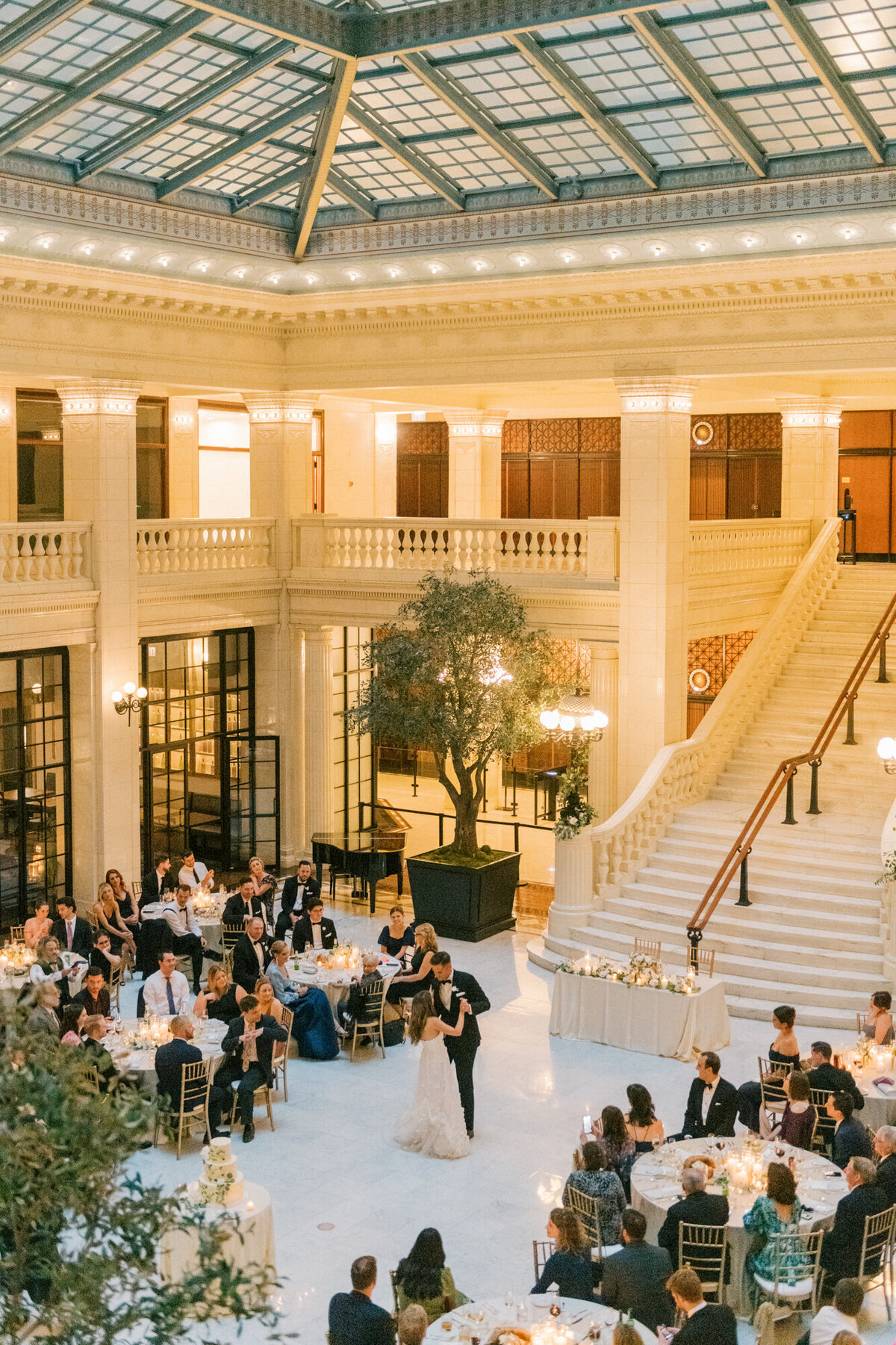 A newlywed couple sharing their first dance in the grand setting of The Exchange in Chicago, surrounded by candlelight and guests.