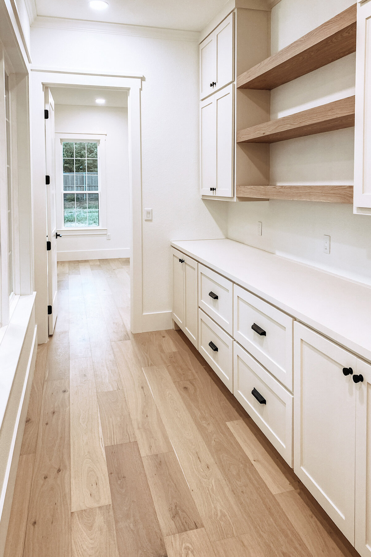 white cabinet built ins with white countertops and wood open shelving in hallway with light wood floors