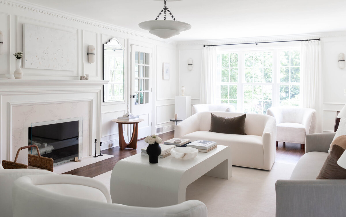 Elegant living room with an all-white color palette, featuring a sculptural coffee table, plush curved sofas, and refined architectural details. A blend of modern and classic design elements creates a sophisticated, airy space. Ideal for luxury home interiors in Short Hills, Montclair, Summit, Chatham, and Ridgewood.