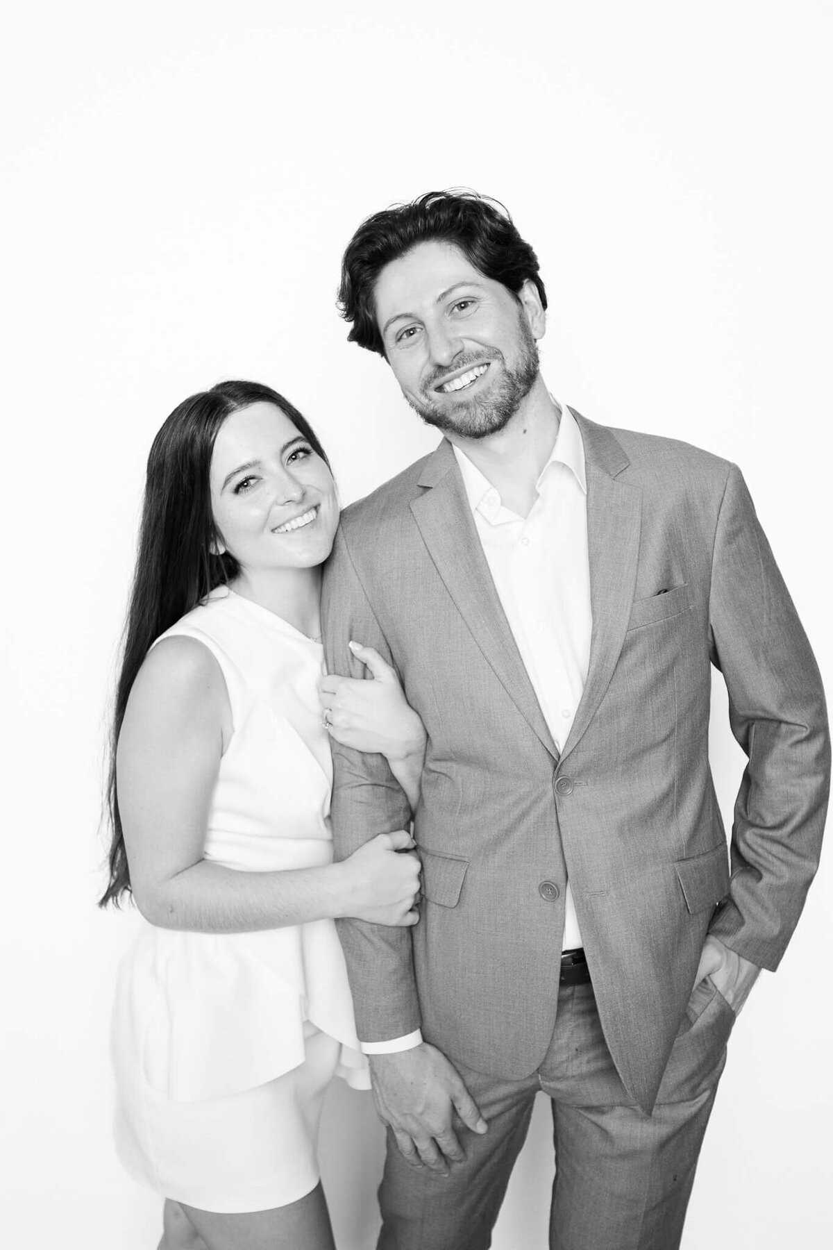 A smiling couple posing together in a bright black and white portrait captured by Monochrome Portraits, a Phoenix photo booth experience focused on modern elegance.