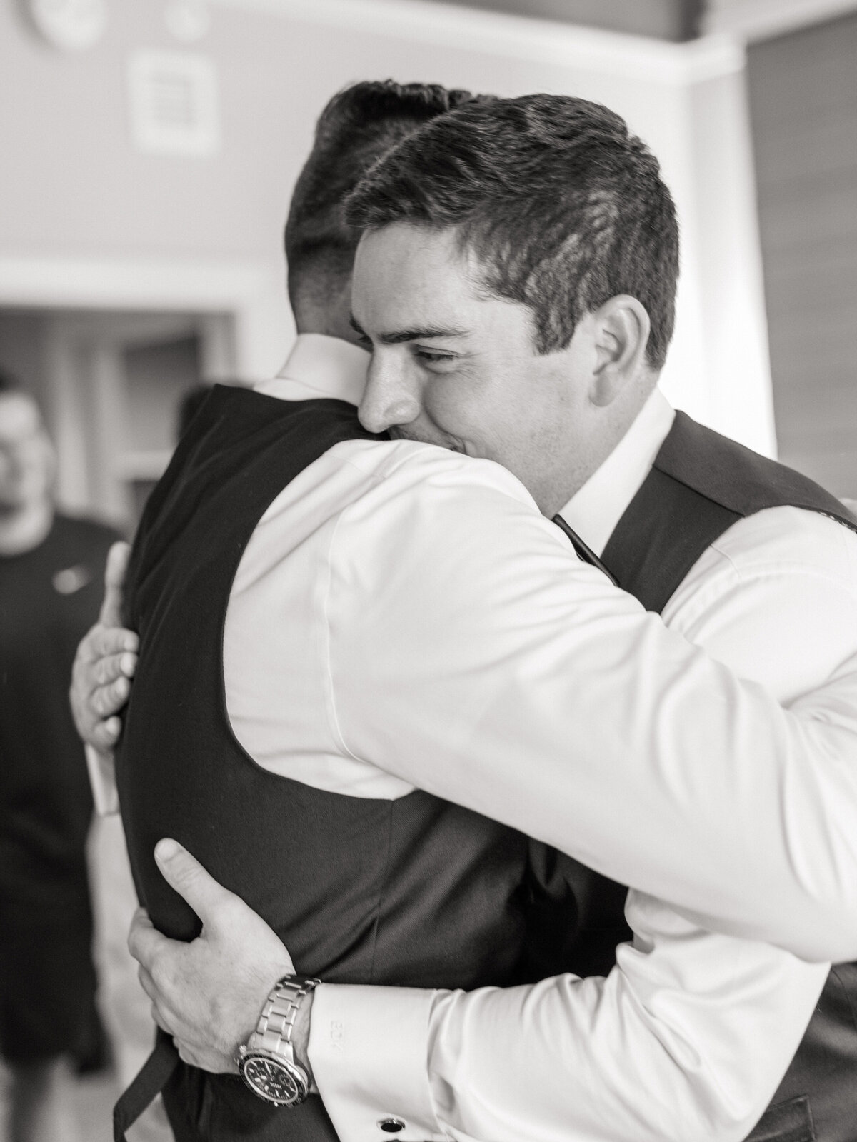 Groom embraces groomsman with a smile before the wedding, captured by a Philadelphia wedding photographer.