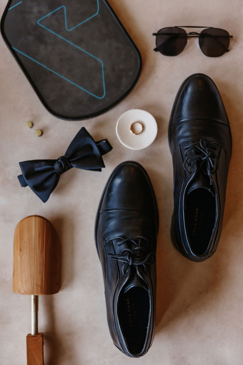groom detail flat lay with dress shoes, shoe expander, bowtie, wedding ring, sunglasses and pickleball paddle