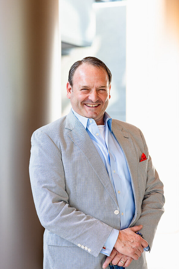 Man in gray jacket smiles in front of gray column.