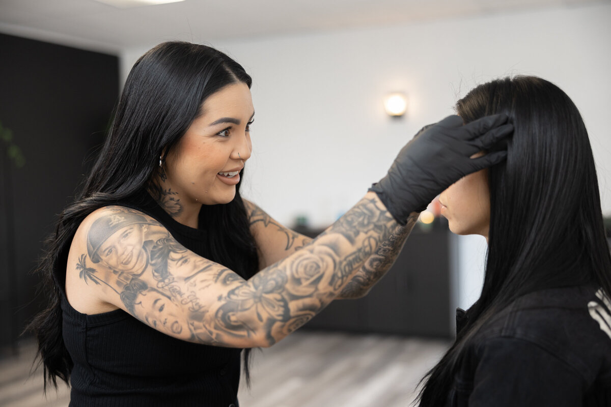 Woman with long dark hair and tattoos styling a client’s hair in a studio. Photograph by Yucaipa branding photographer Kaitlyn Dawn Photography.