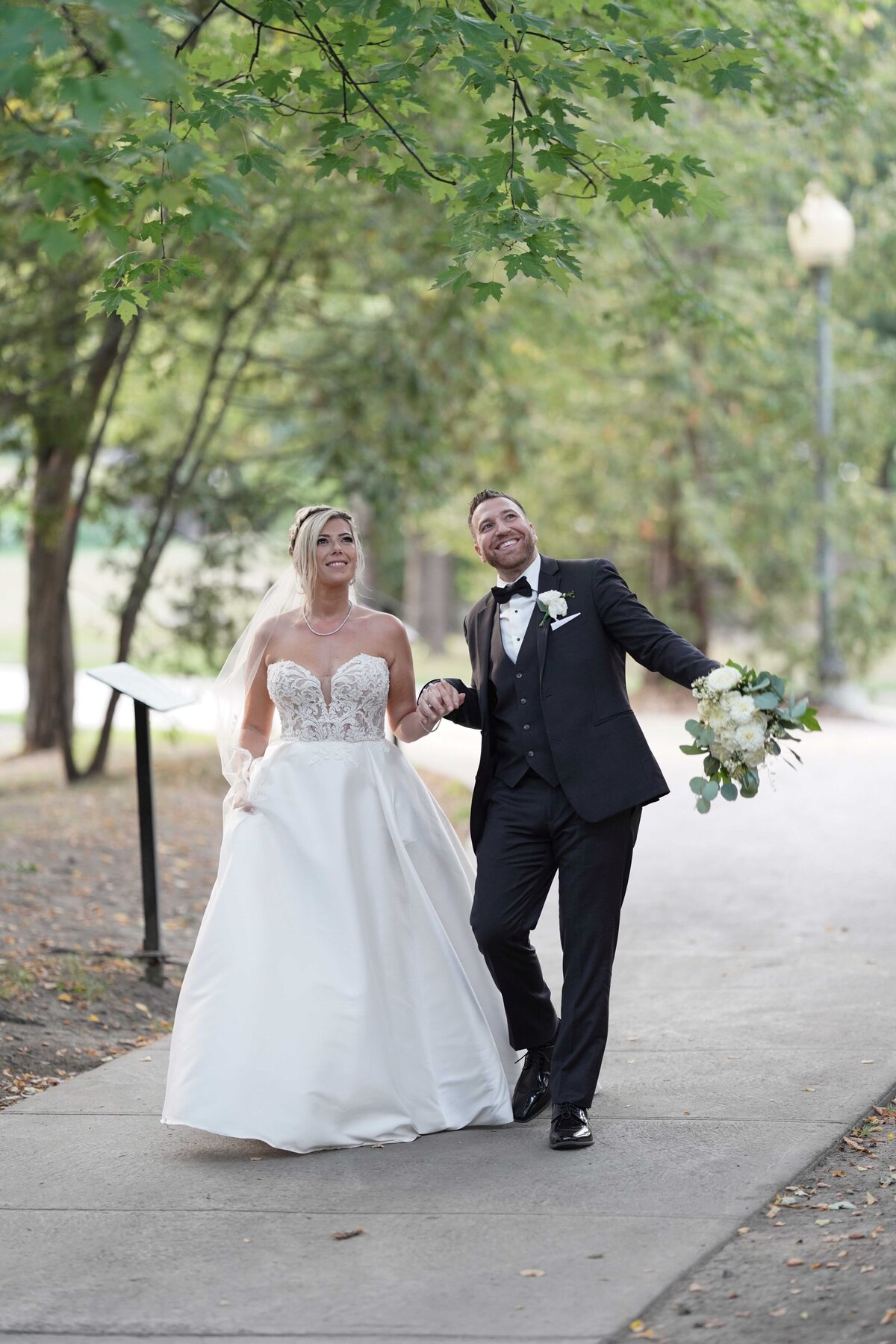 A couple strolls down the sidewalk, holding hands and smiling at each other. The image captures their joyful connection and carefree love as they enjoy a sunny day together.