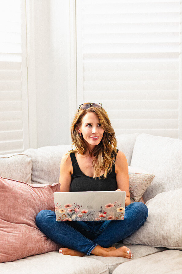 Girl sits on couch with laptop in her lap and looks off to the side.