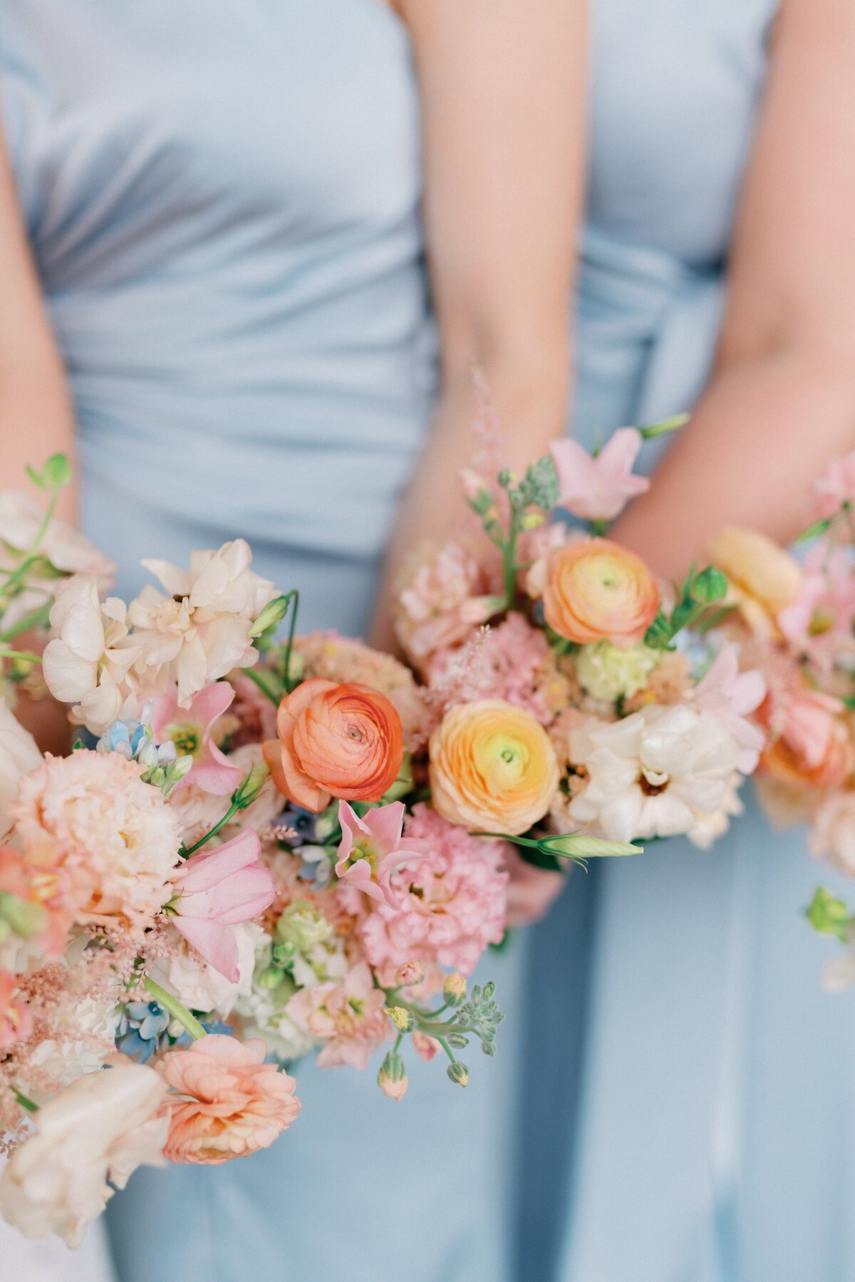 Colorful bouquets bursting with spring colors held by bridesmaids in soft blue dresses taken by Illinois wedding photographer Lacey Graham