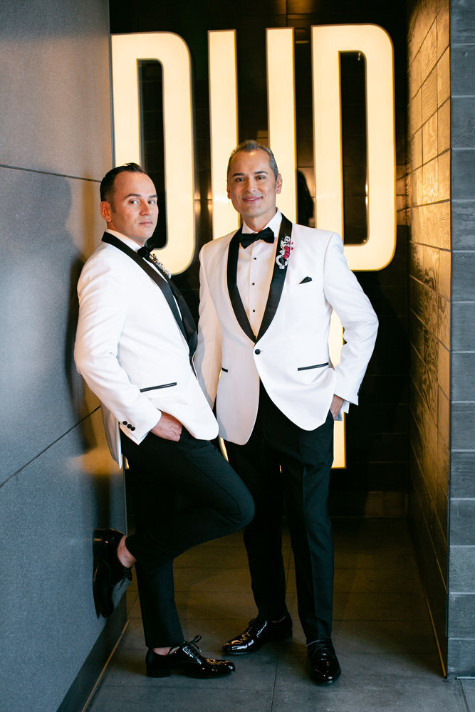 A groom leaning on a wall with another groom standing behind him