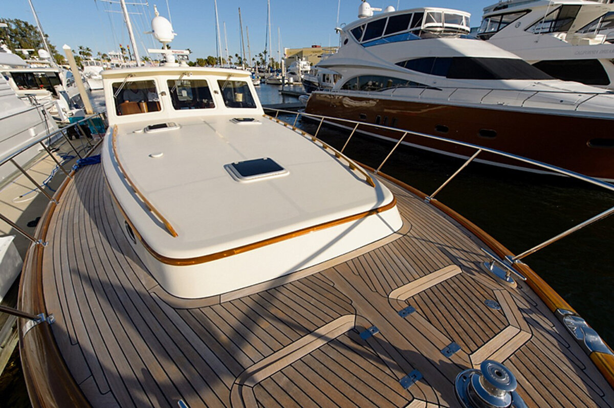 A close-up of a yacht's spacious deck, featuring polished wooden flooring and stainless steel railings, surrounded by other luxury boats under a clear blue sky
