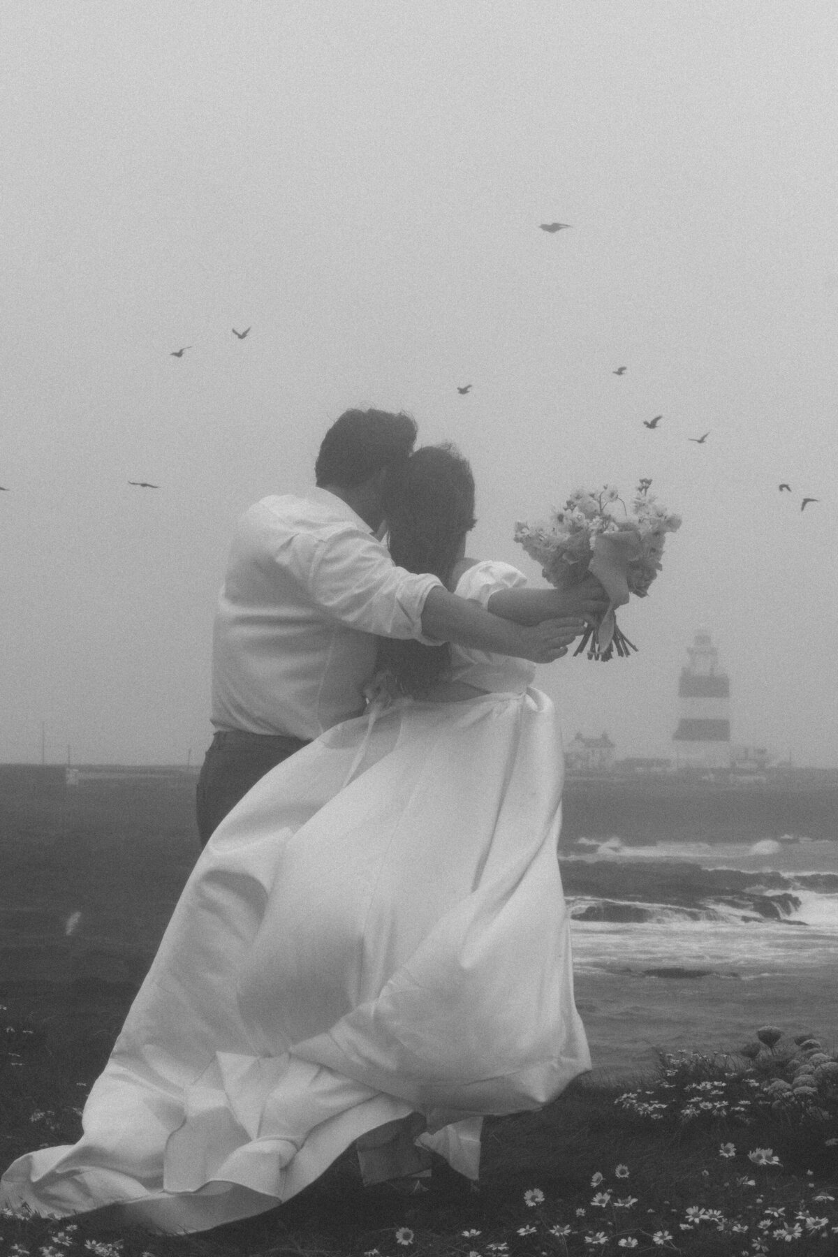 newly married couple holding each other in a field with a flock of birds 