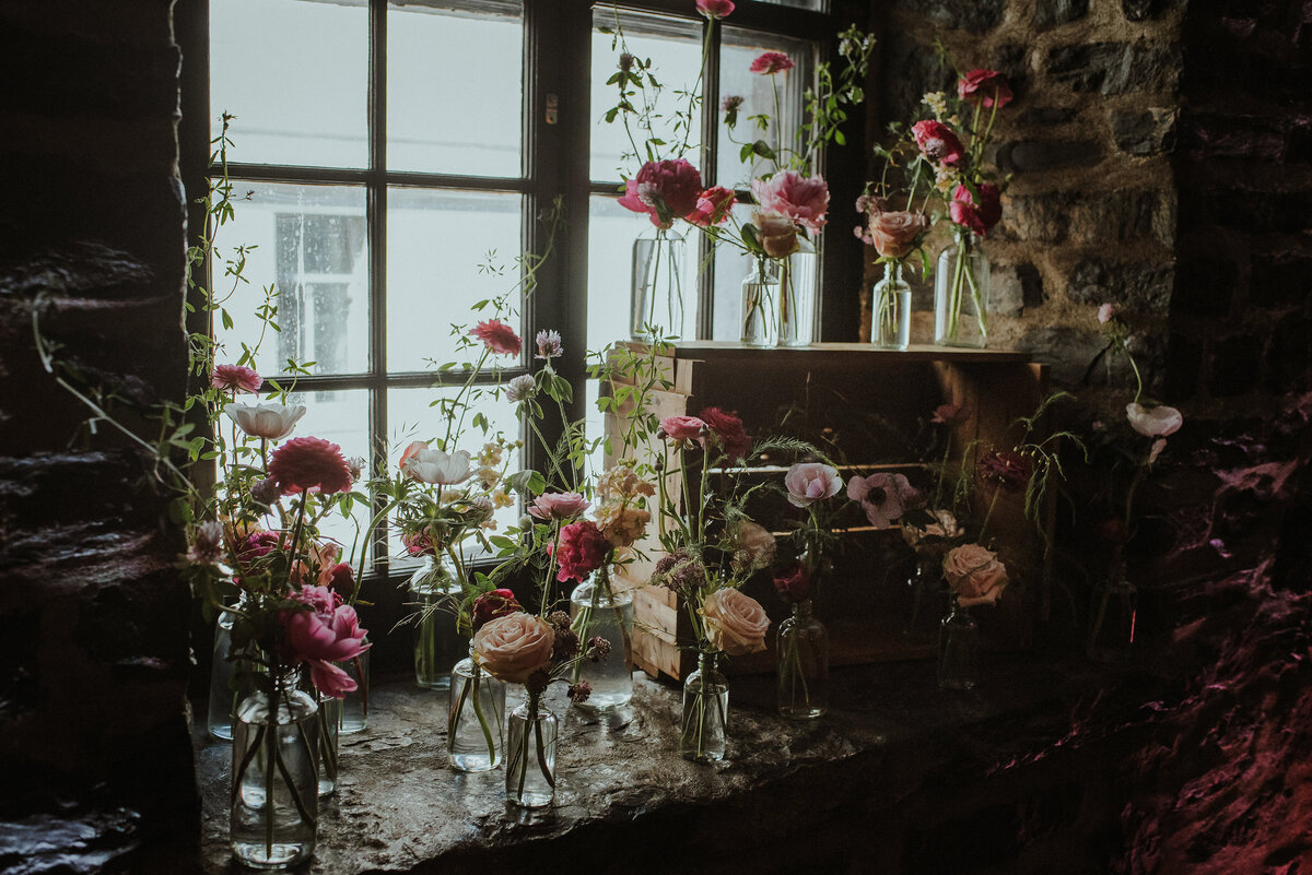 An array of bud vases with pink flowers sit in a stone window sill before a Montreal wedding. 
