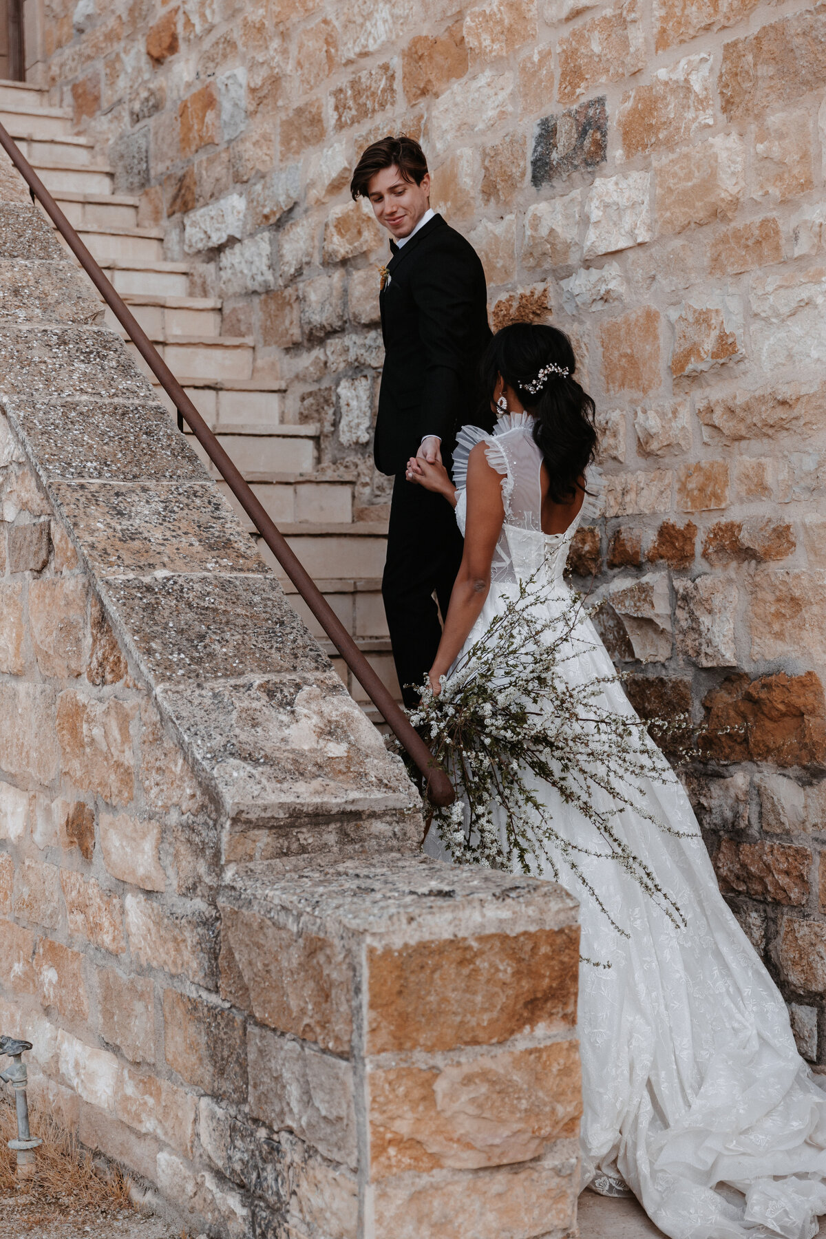 Bride holding a wildflower bouquet walks up rustic stone stairs with the groom at Sunstone Winery.