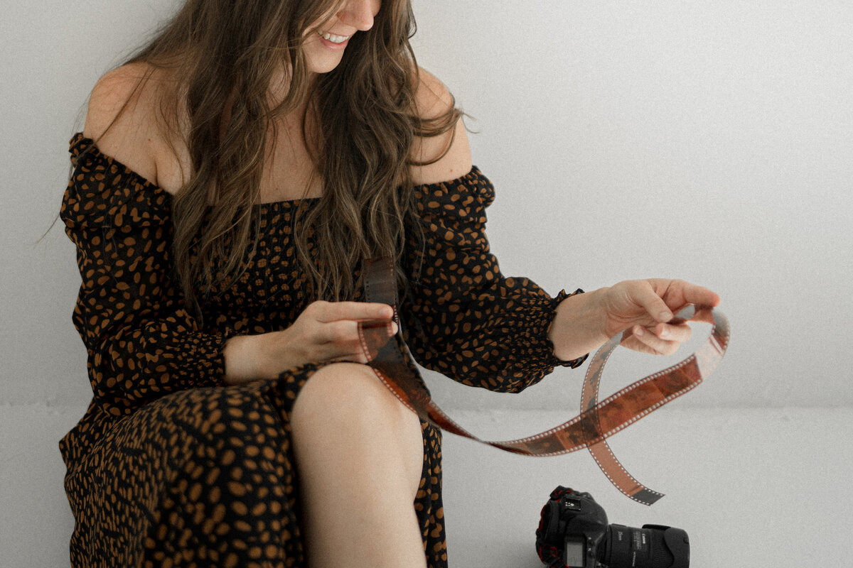 closely cropped photo of Nicole sitting on the ground indoors while holding and inspecting a roll of developed 35mm film
