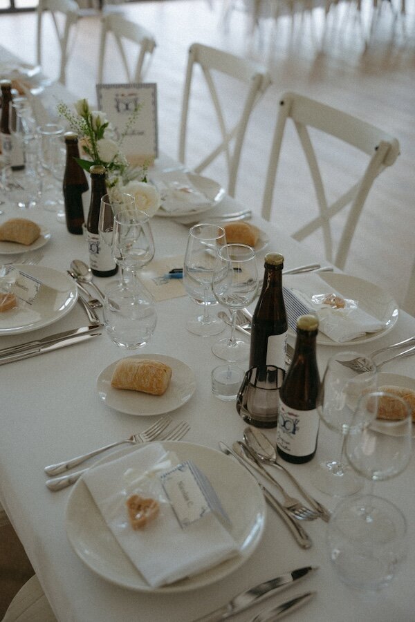 Élégante table de réception dressée avec détails raffinés, vaisselle soignée et bières artisanales. Un mariage blanc et épuré capturé par Kamescop.