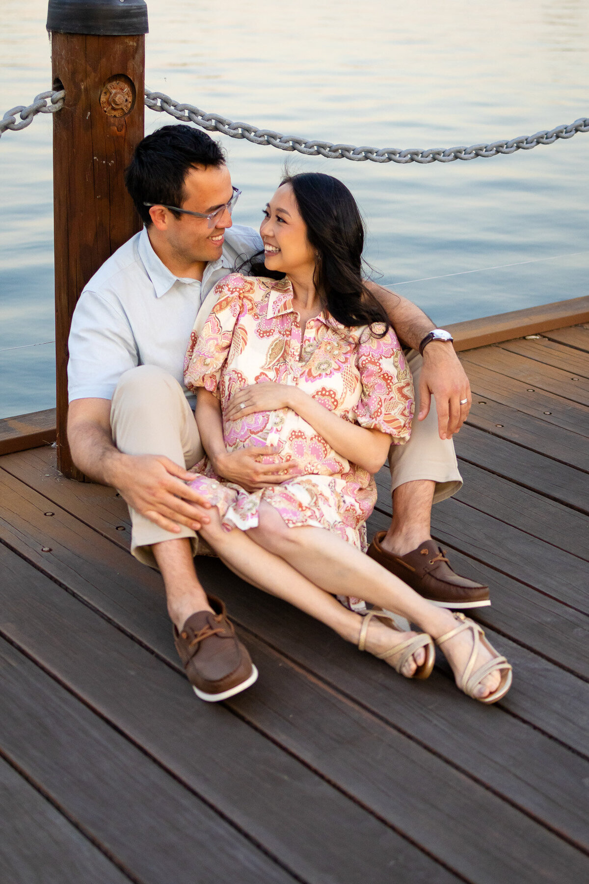 Maternity couple laughing and holding each other by the water on a wooden dock, featured in Bay Area Maternity Portfolio - Ellobelle Photography
