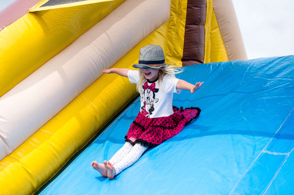 a little girl in a red skirt sliding down an inflatable slide.  Captured by Ottawa Event Photographer JEMMAN Photography COMMERCIAL during a corporate children's event