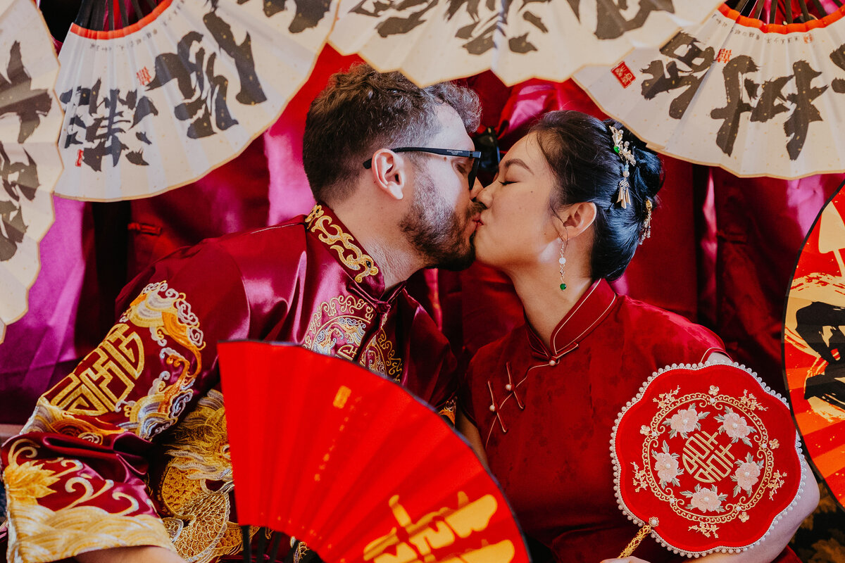 Bride and groom in traditional Chinese attire kissing surrounded by fans, wedding photographer Tuscany.