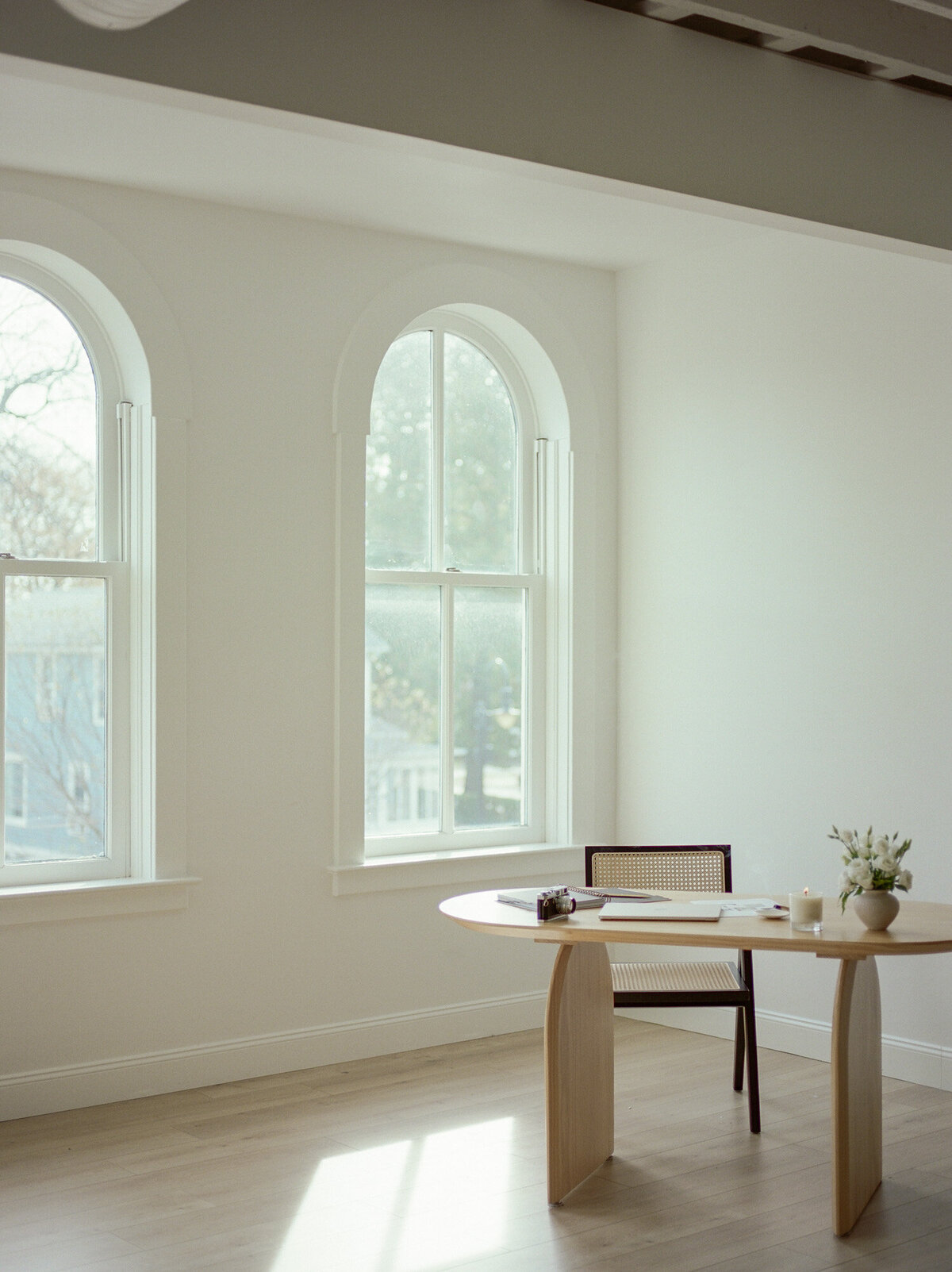 wood desk, wood chair with black trim, arched windows in clean, white, natural light studio for branding photography
