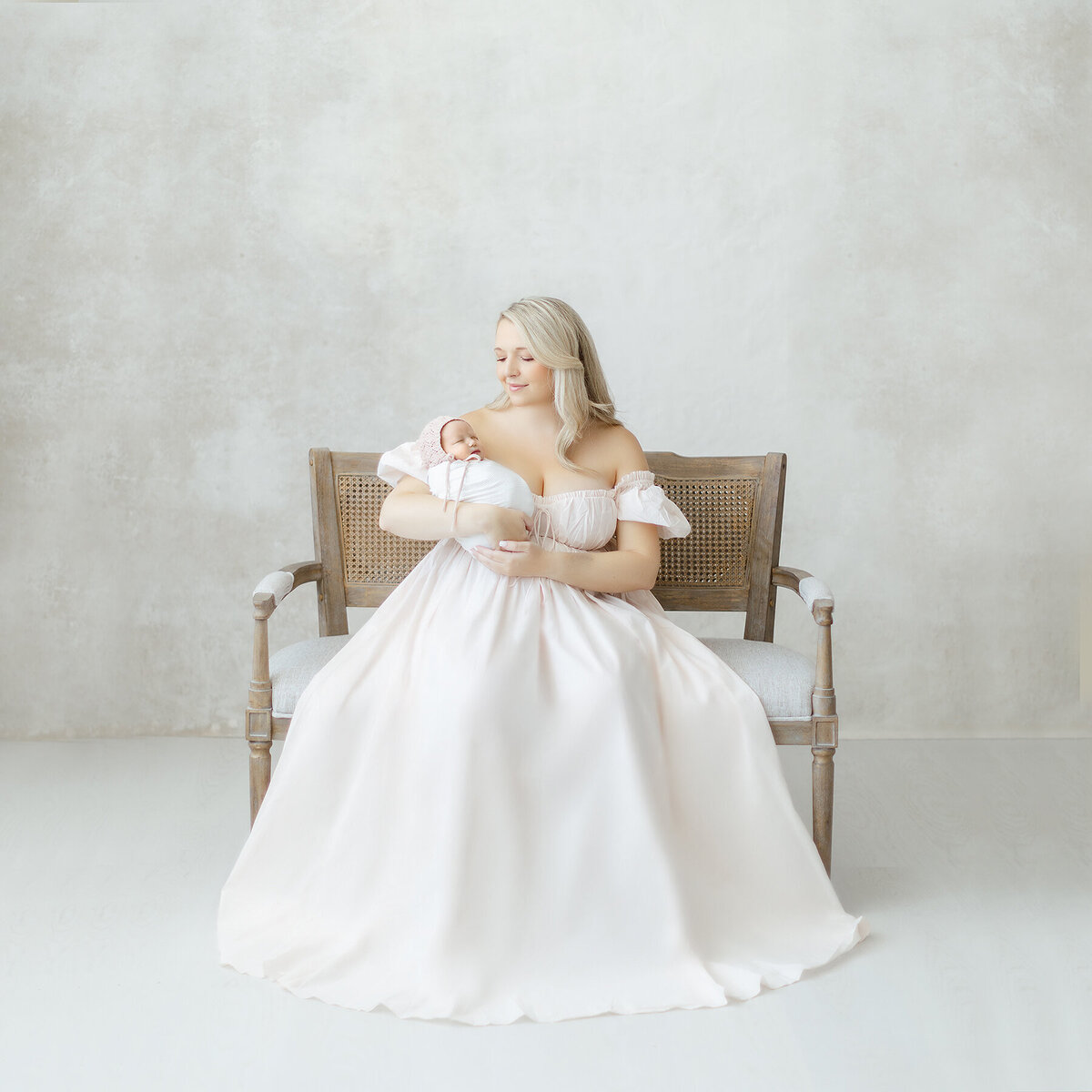 Elegant newborn photo taken in a DFW photography studio of a mother sitting on a chair while she holds her newborn baby girl.