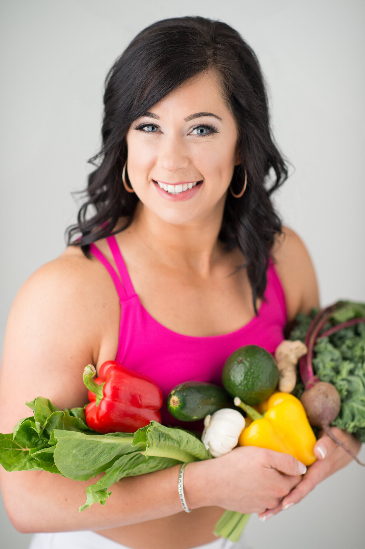 closeup branding photo of a personal trainer in her workout gear holding and armful of healthy vegetables