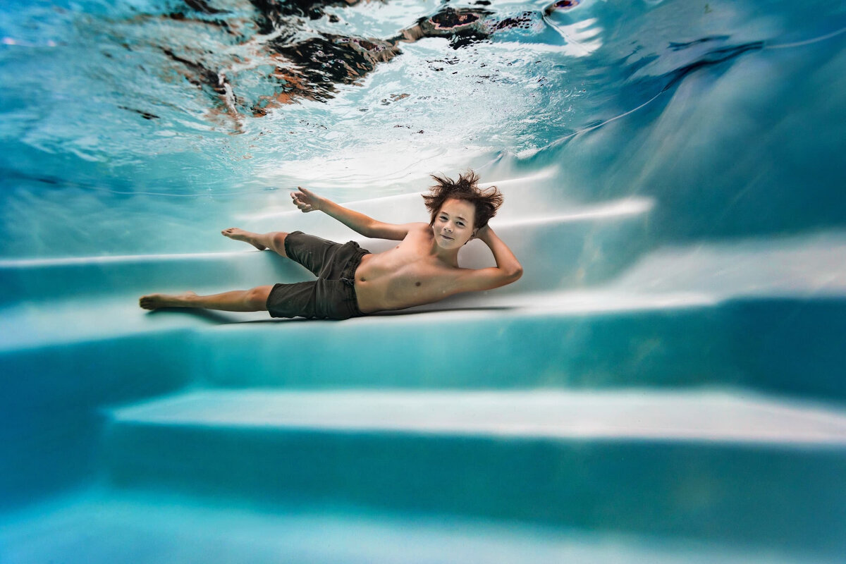 portrait jeune homme souriant allongé sur une marche sous l'eau en piscine l'air détendu