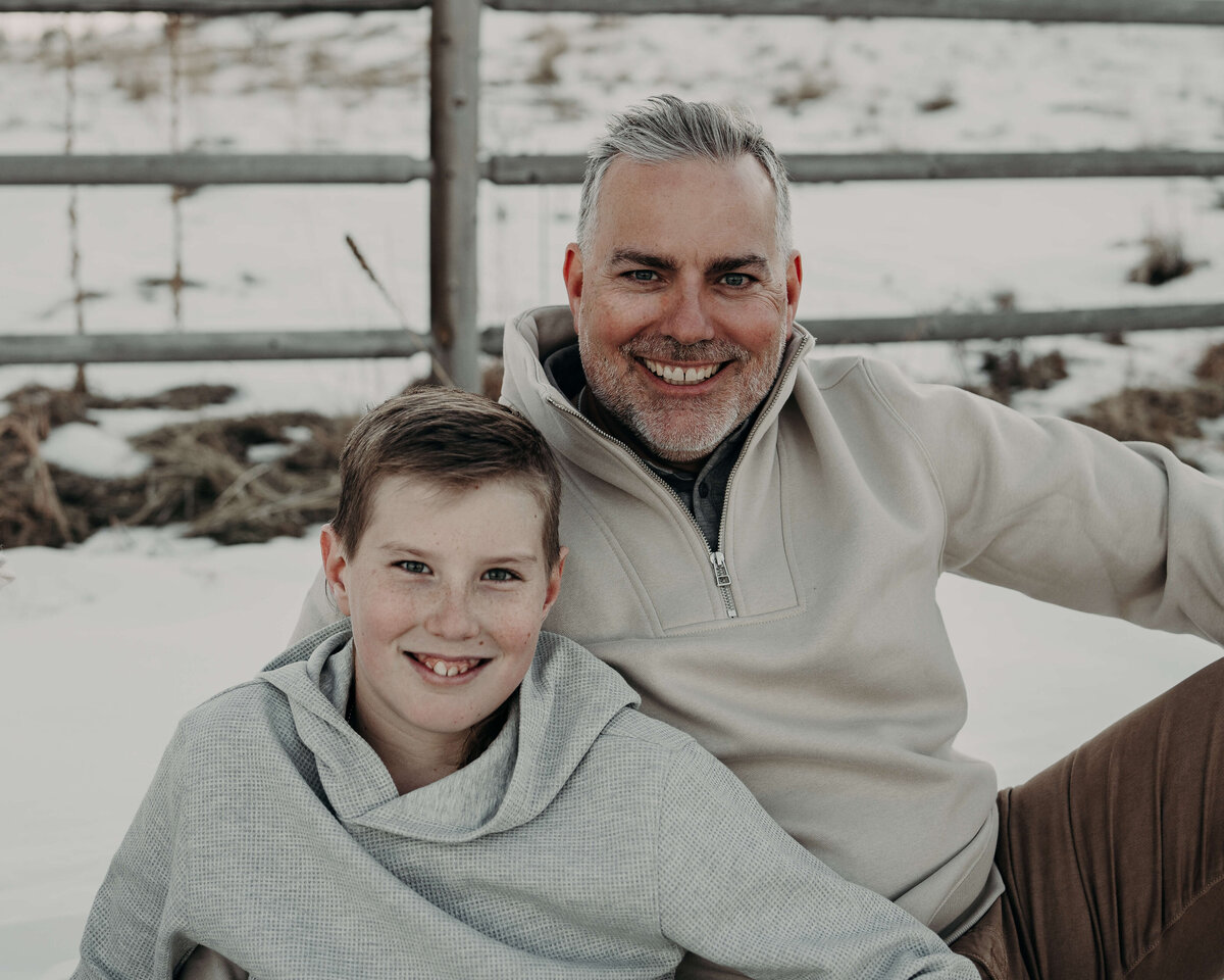 A portrait of a father and son, wearing coordinating sweaters during a winter photography session with snow in the background.