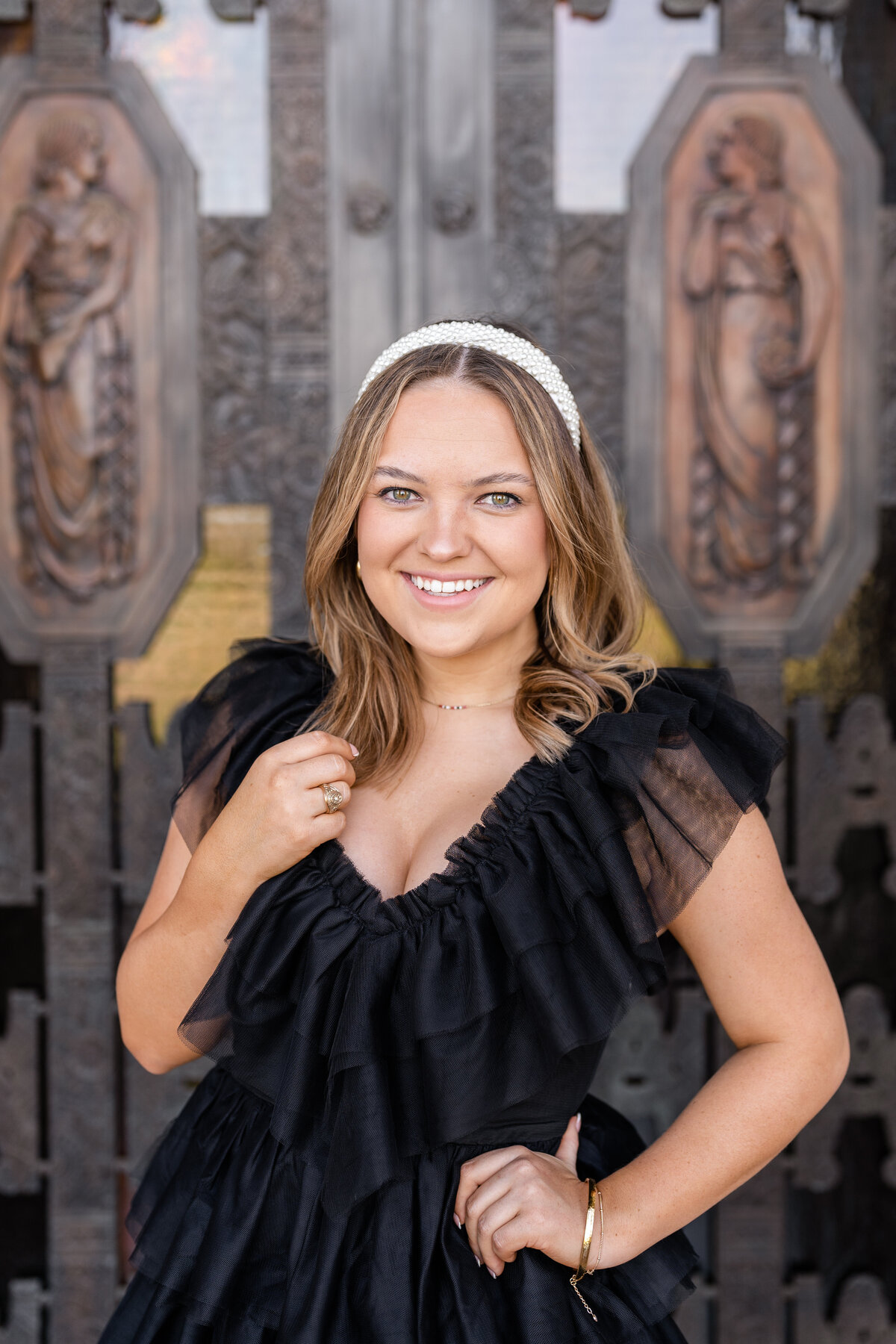 Texas A&M senior girl smiling in front of Administration Building front door wearing a fluffy black dress and pearl headband
