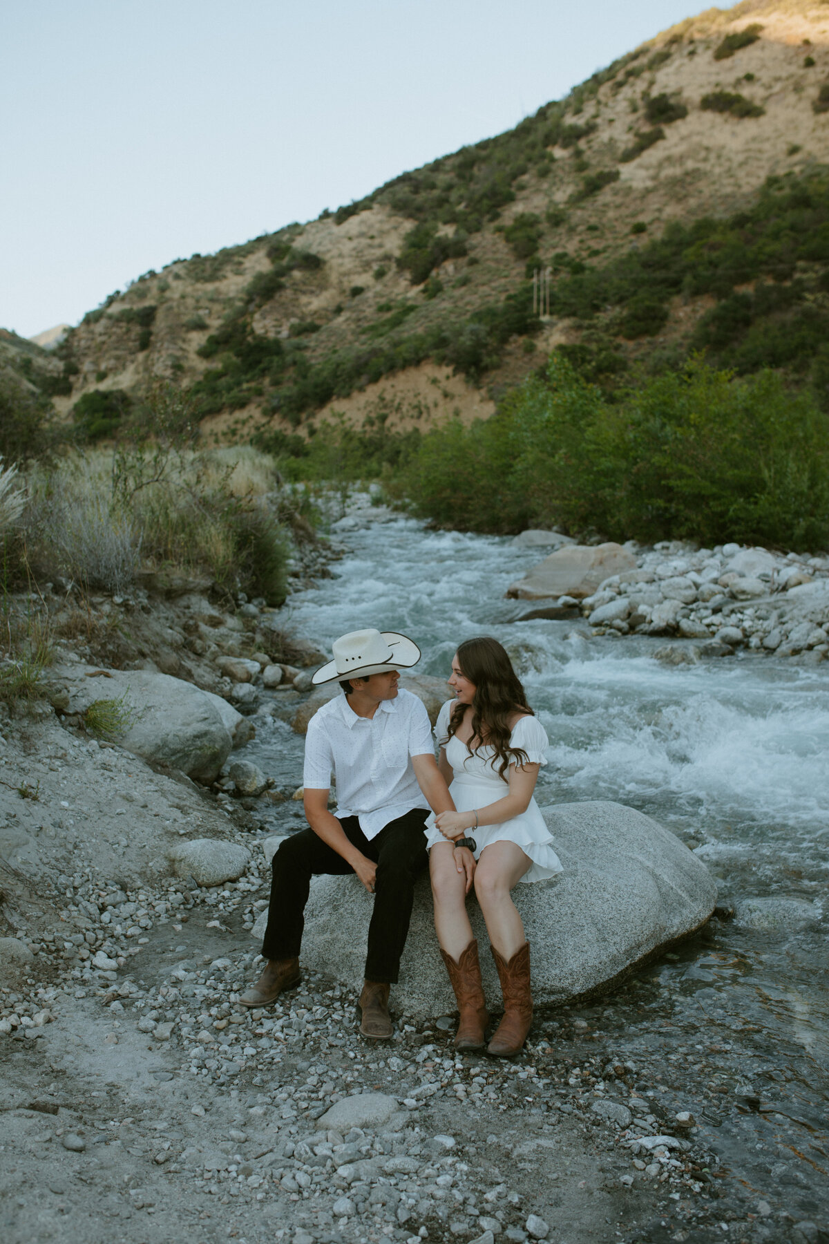 couple sitting on rock holding hand with moutains in the backround